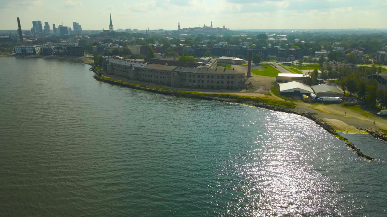 Aerial drone footage flying closer to a old historic sea fortress on the Baltic sea shoreline. The patarei former prison building is surrounded by grassy shores and cityscape is visible in the back