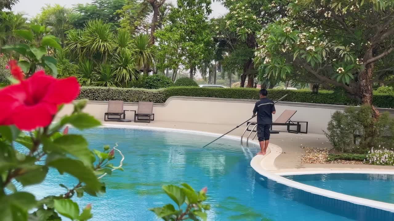 A tranquil poolside scene in Champasak, Laos, featuring lush greenery and vibrant red flowers under soft daylight