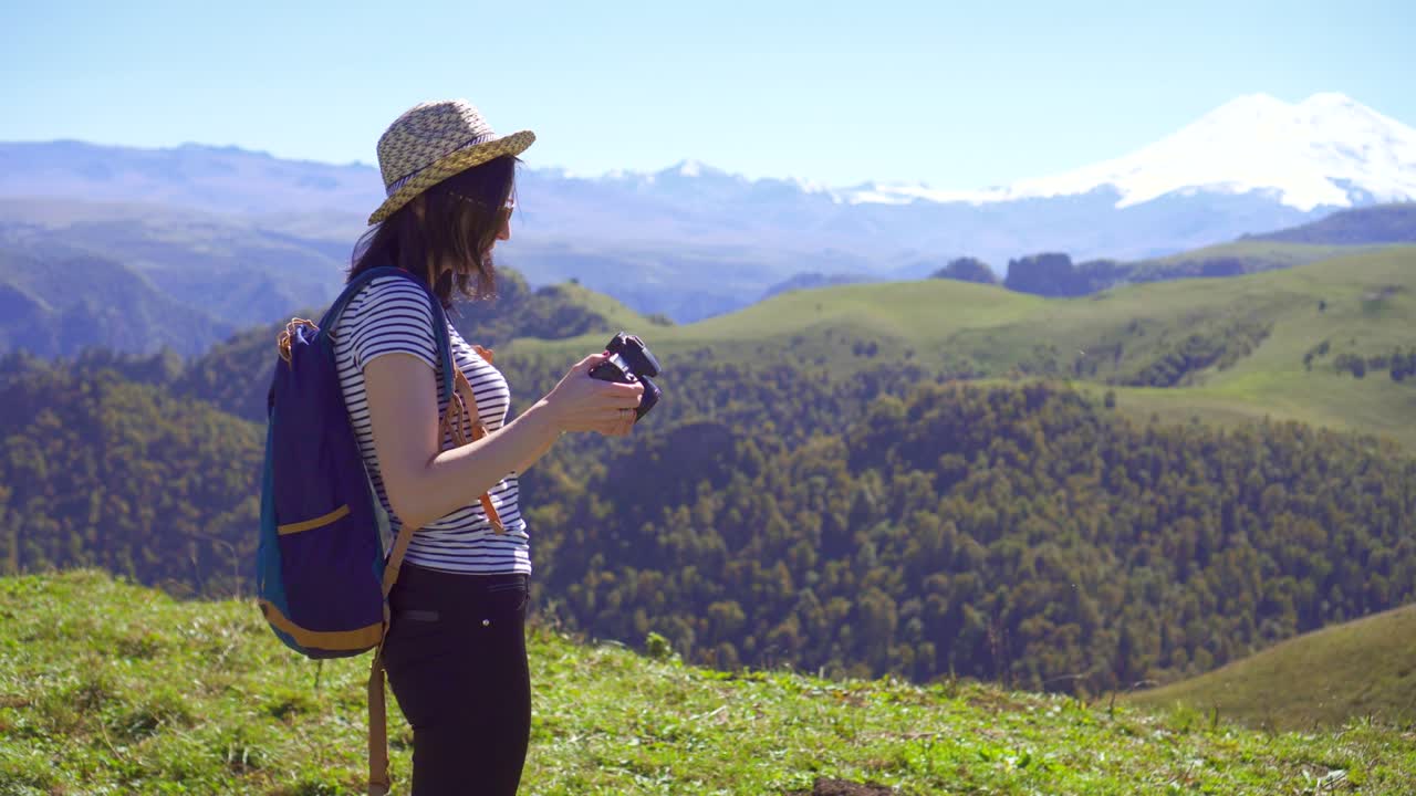 배을 들고 있는 소녀의 뒷면은 디지털 카메라로 산의 사진을 찍습니다.