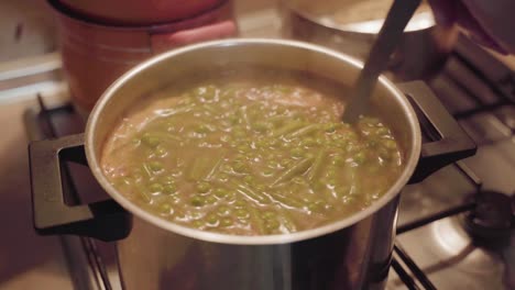 mano con cucharón revolviendo sopa de guisantes cocinando en estufa de gas