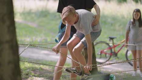 children on a summer camp hike are moving along the ropes with the help of a guide who teaches children rock climbing and tourism. a boy in the forest overcomes a rope barrier