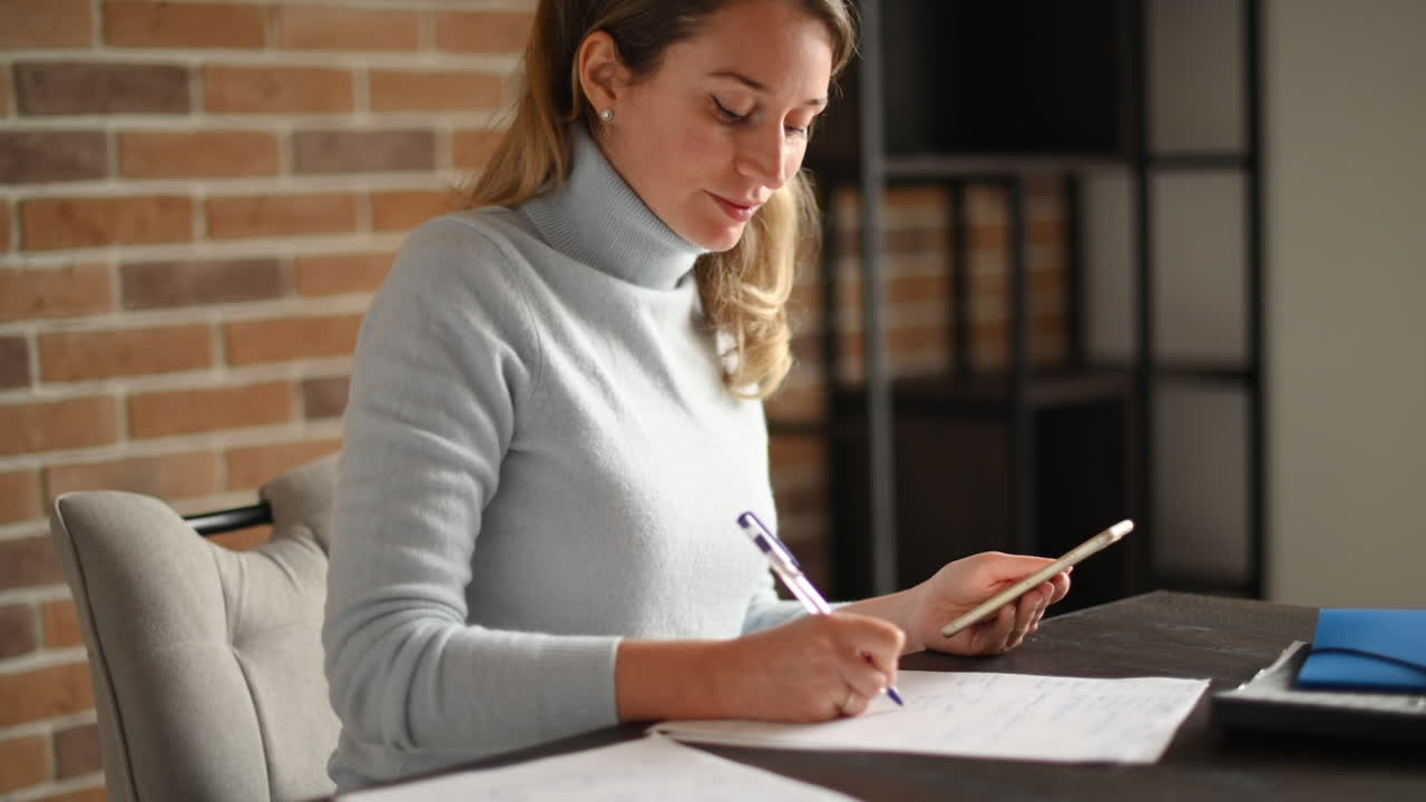 Woman working on mobile phone and writing at the office