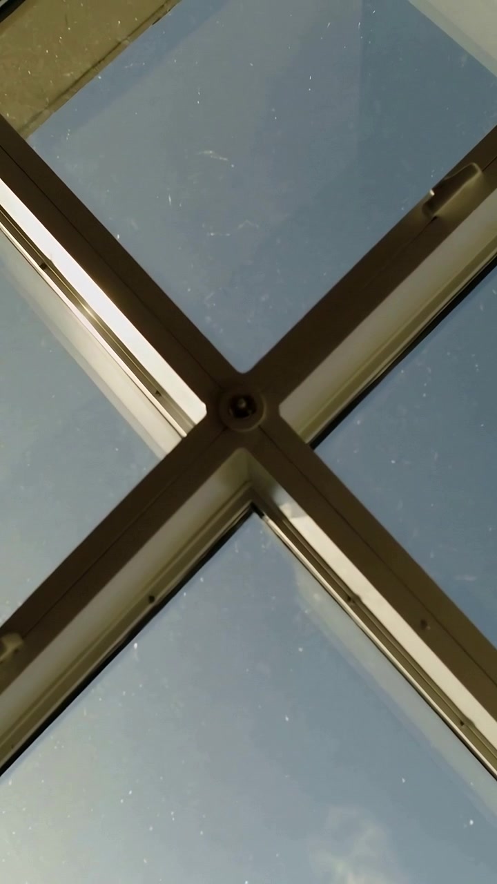 Video verticale: Telecamera che si inclina inquadrando un telaio a X di lucernario sulla linea del tetto, centrando un bullone e mostrando la polvere.