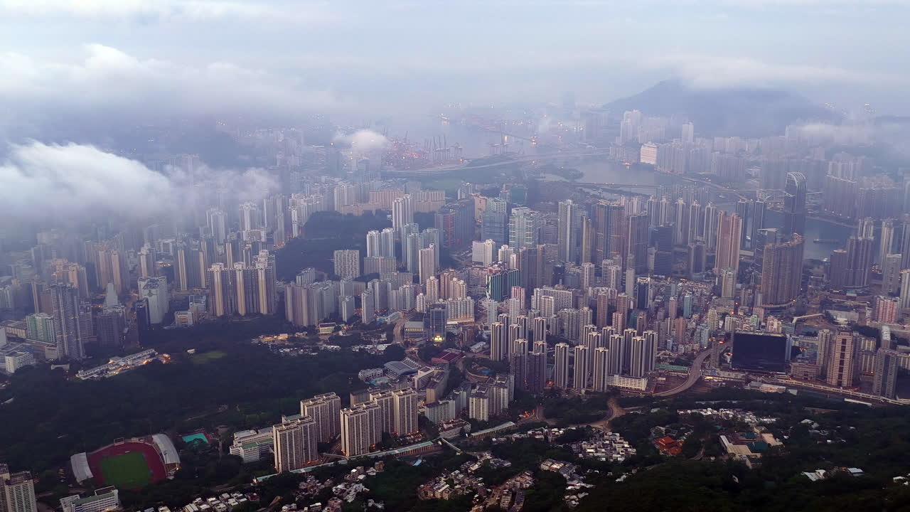 Cinematic aerial view of Hong Kong skyline shrouded in mist at blue hour, with glowing skyscrapers and Victoria Harbour fading into a moody, atmospheric twilight