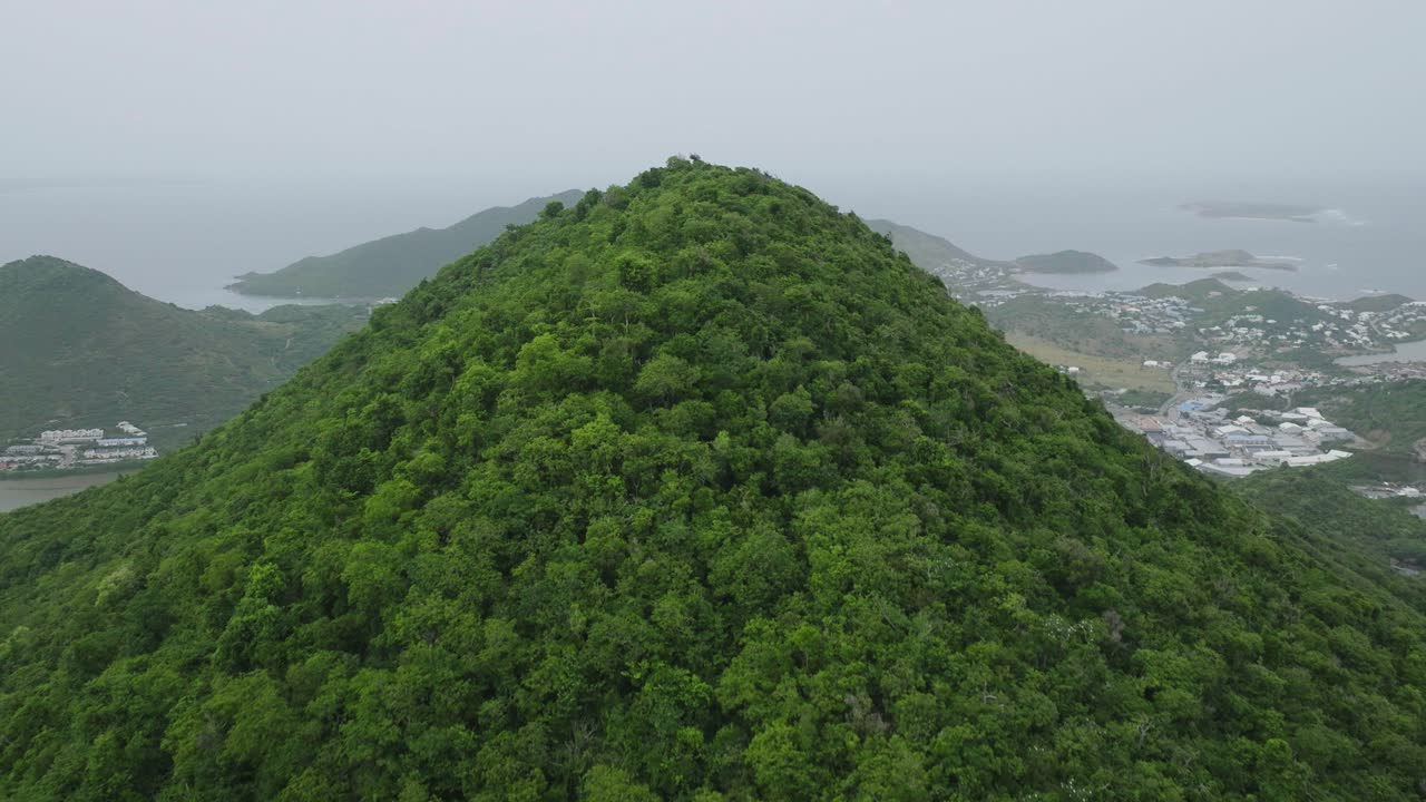 Drone flying through mountains filled with greenery of Saint Martin during cloudy day in Carribean Island. Townscape.