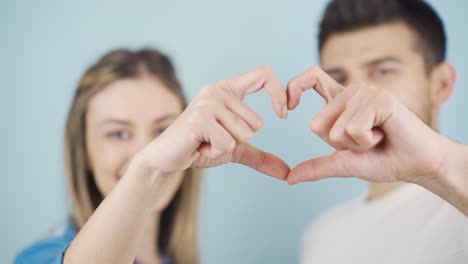 una feliz pareja casada haciendo corazones y mirando a la cámara.