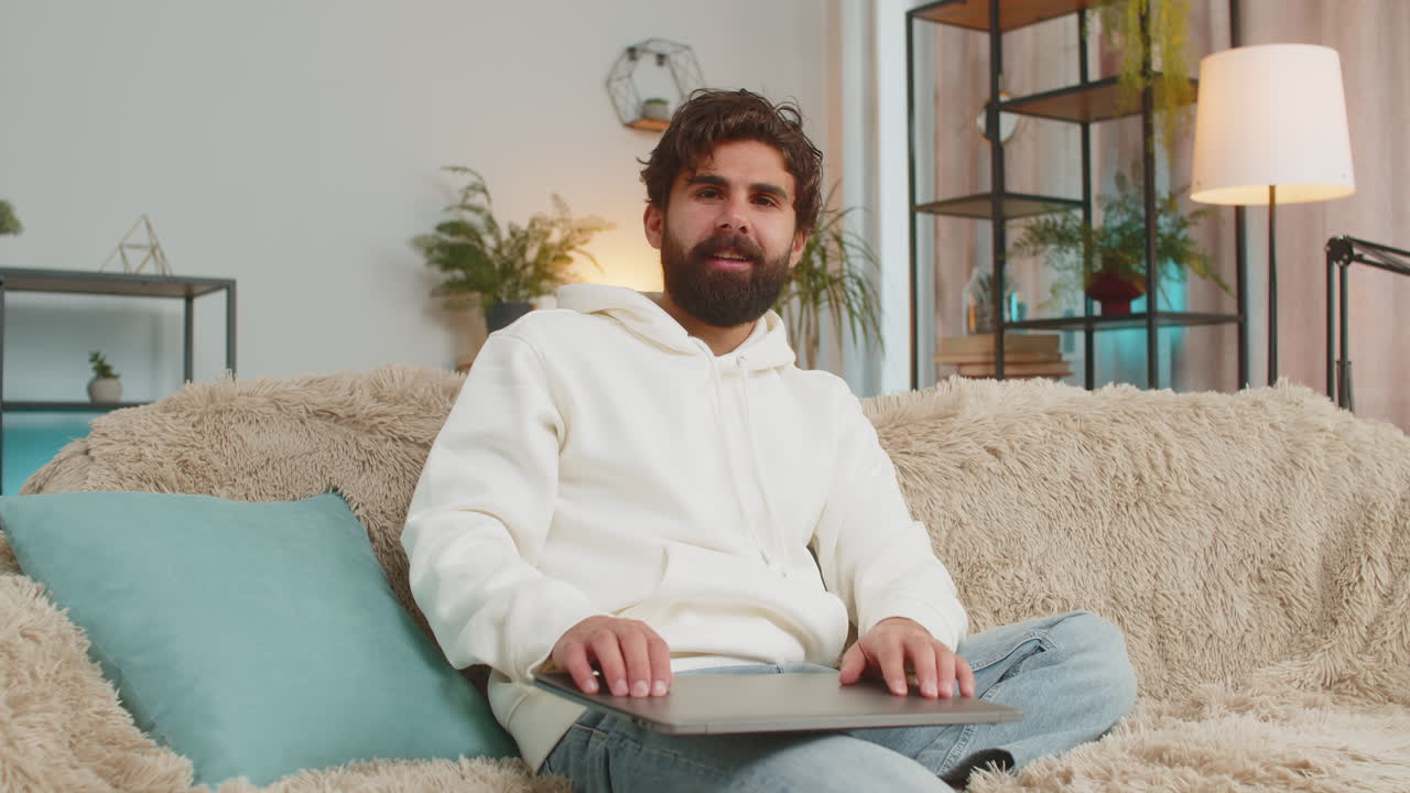 Happy indian man freelancer sitting on couch closing laptop after finishing work in living room
