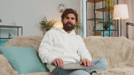 happy indian man freelancer sitting on couch closing laptop after finishing work in living room