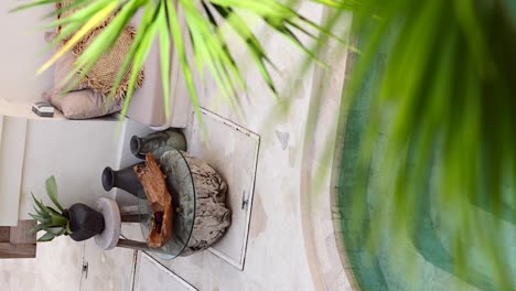 vertical - courtyard terrace in bali tropical villa by the pool decorated in boho style - tilt up revealing from behind palm leaf