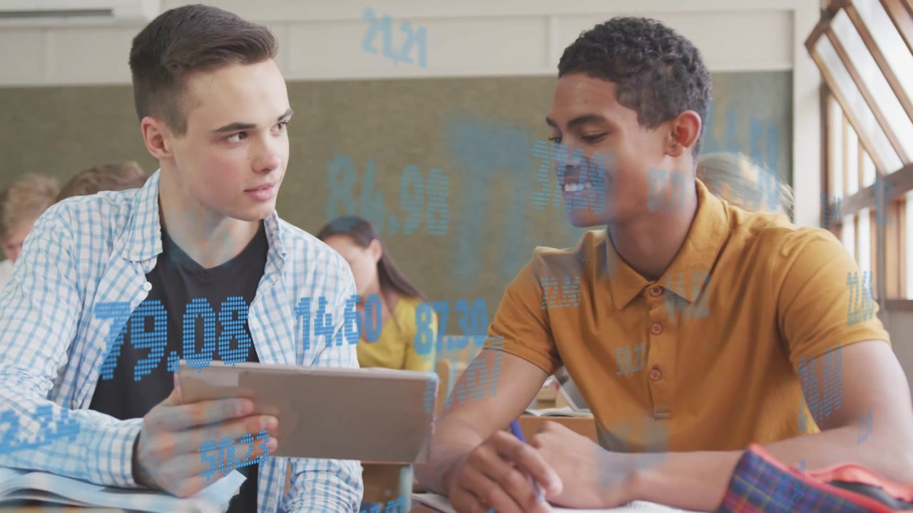 Student pair showing tablet in classroom, leaning and pointing at blue overlay, then writing notes