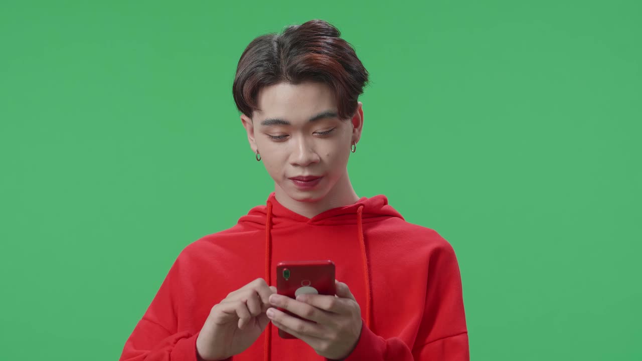 Happy Young Asian Transgender Male Use Mobile Phone While Standing On Green Screen In The Studio