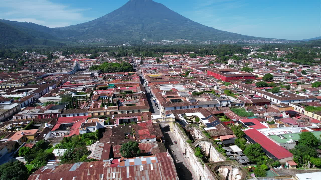 Aerial view: Santa Catalina Arch, Antigua Guatemala, with red rooftops, volcano, and sunny day