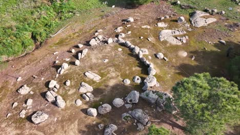 Orbital-flight-with-a-drone-over-a-cromlech-with-a-circular-shape-of-granite-stones,-it-is-fenced-with-ropes-to-prevent-its-access,-surrounded-by-trees-and-vegetation-in-Toledo,-Spain