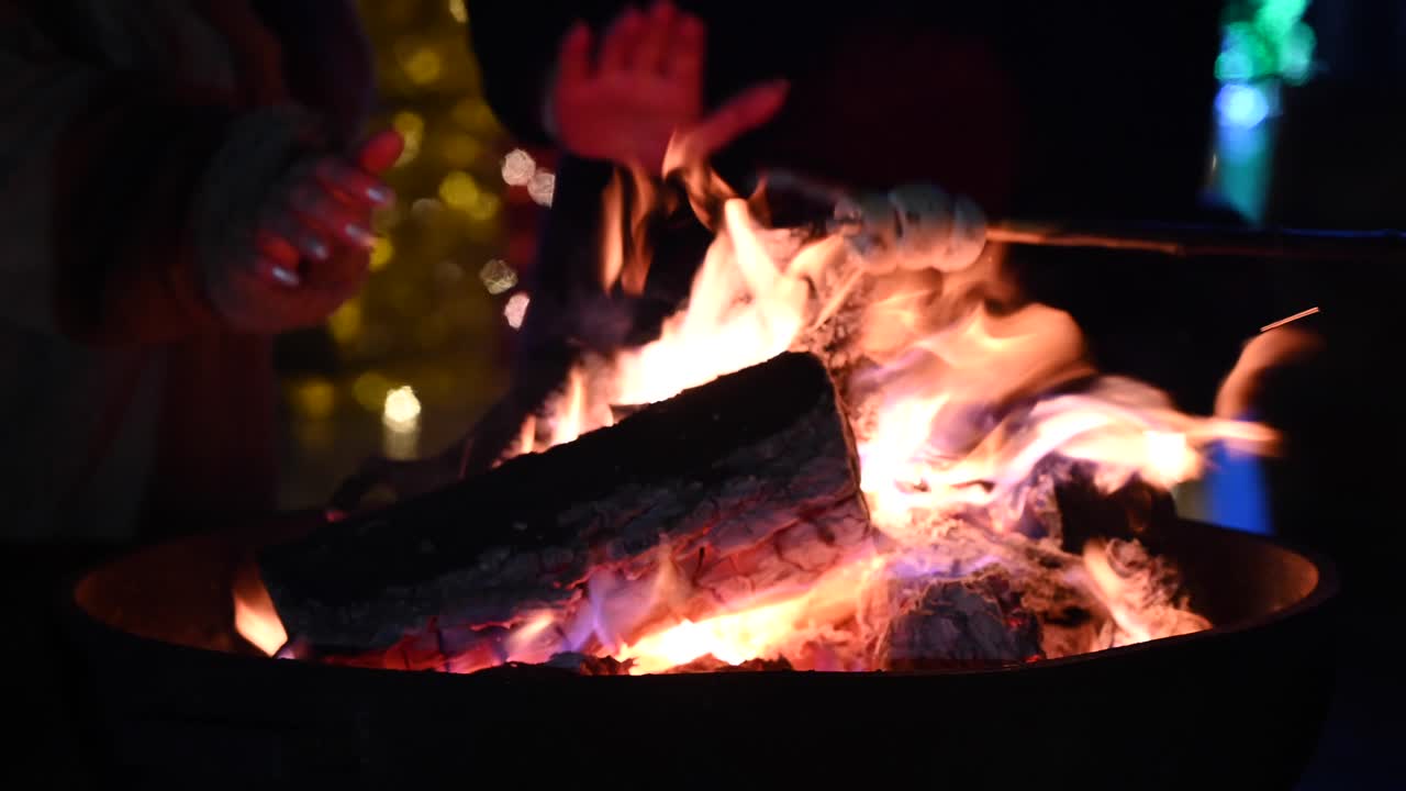 Close up of people warming their hands on a fire burning outside