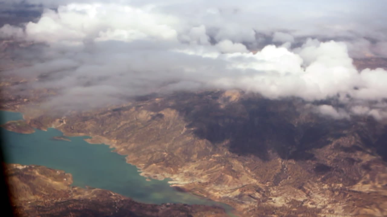 Aerial view of a cloudy mountain landscape with a turquoise lake below