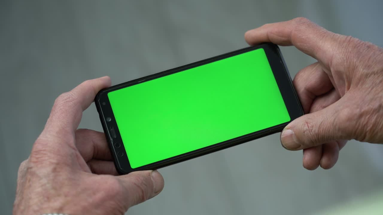 Elder person holding in wrinkled hands black phone with chroma key