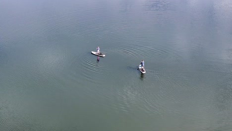 aerial-orbit-around-two-people-paddleboarding-on-a-lake-mid-day-4k