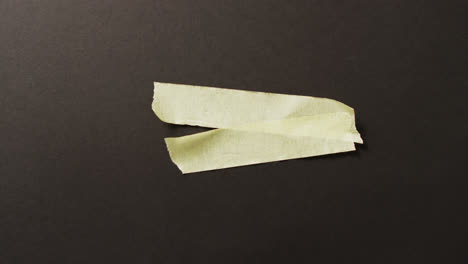 Video-of-close-up-of-two-yellow-paper-tape-pieces-on-black-background