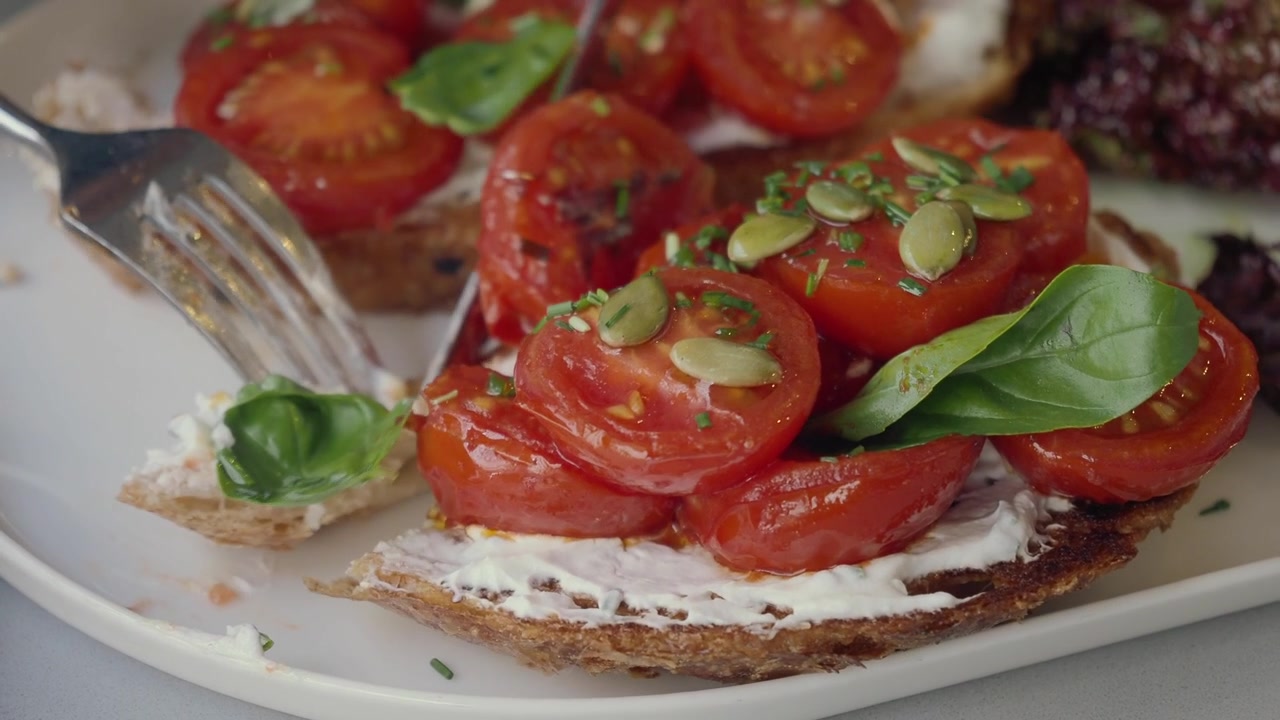 Close de uma pessoa cortando uma bruschetta de tomate e cream cheese