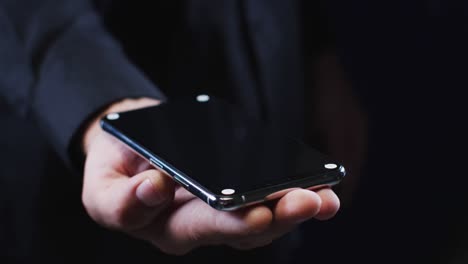 hand of a caucasian man wearing a black shirt cradling a smartphone