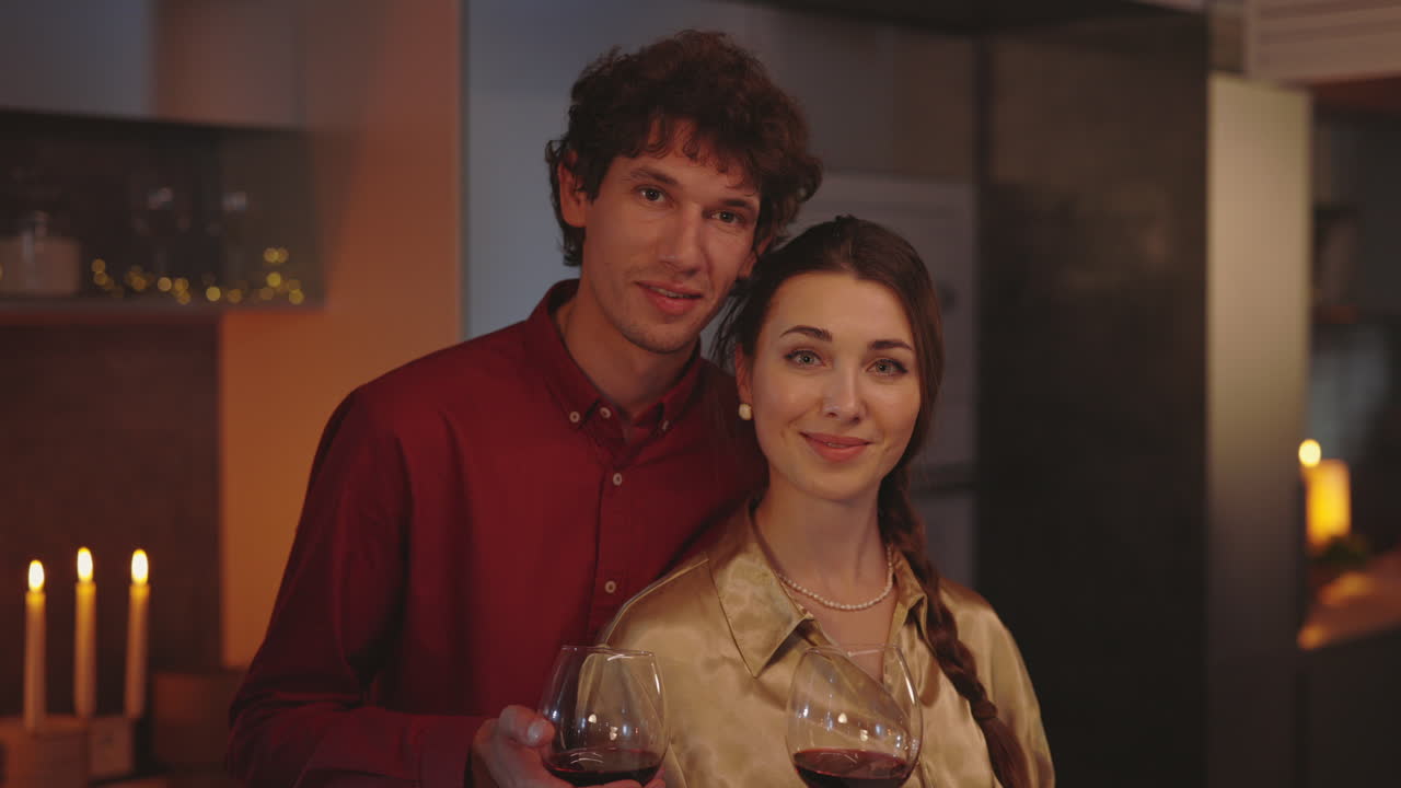 Couple toasting with red wine in a cozy indoor setting with candlelight