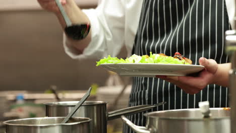 chef pouring sauce on top of salad on a plate in the kitchen of a restaurant