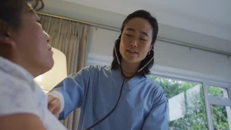 Doctora-Asiática-Sonriente-Usando-Estetoscopio-Examinando-A-Una-Paciente-Acostada-En-La-Cama-En-El-Hospital