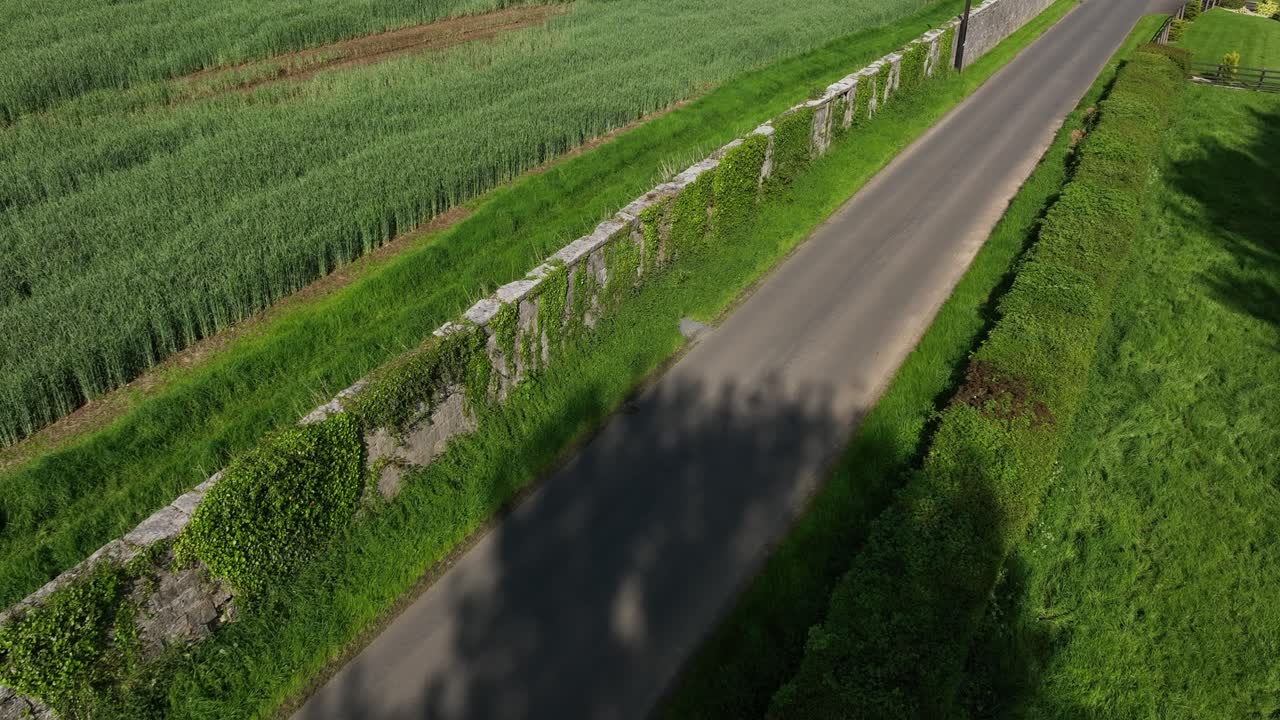 Caledon Border Wall, County Tyrone, Northern Ireland, May 2023. Drone pullback slowly over historic divide wall beside rural road and fields, aerial view of historic countryside divides and farmland.