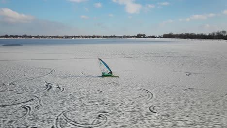 Ice Sailor surfing on snowy covered ice lake in Netherlands during wintertime - aerial track shot