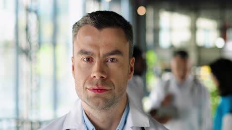 portrait of handsome male physician in white gown looking at camera and standing in clinic