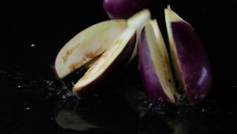 Water-drips,-followed-by-falling-sliced-eggplants-which-separates-on-a-black-background