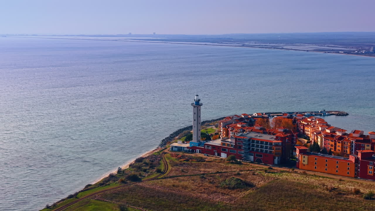 Allontanamento dal faro con torre quadrata adiacente al complesso di case colorate. Paesaggio marino del Mar Nero sullo sfondo. Vista aerea