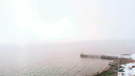 Aerial-view-through-blizzard,-towards-a-pier,-on-the-coast-of-the-arctic-ocean,-foggy-winter-day,-in-Nordland,-North-Norway---dolly,-drone-shot