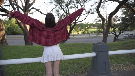 Back-view-of-pretty-woman-raising-her-arms-expressing-freedom-in-park-at-sunset