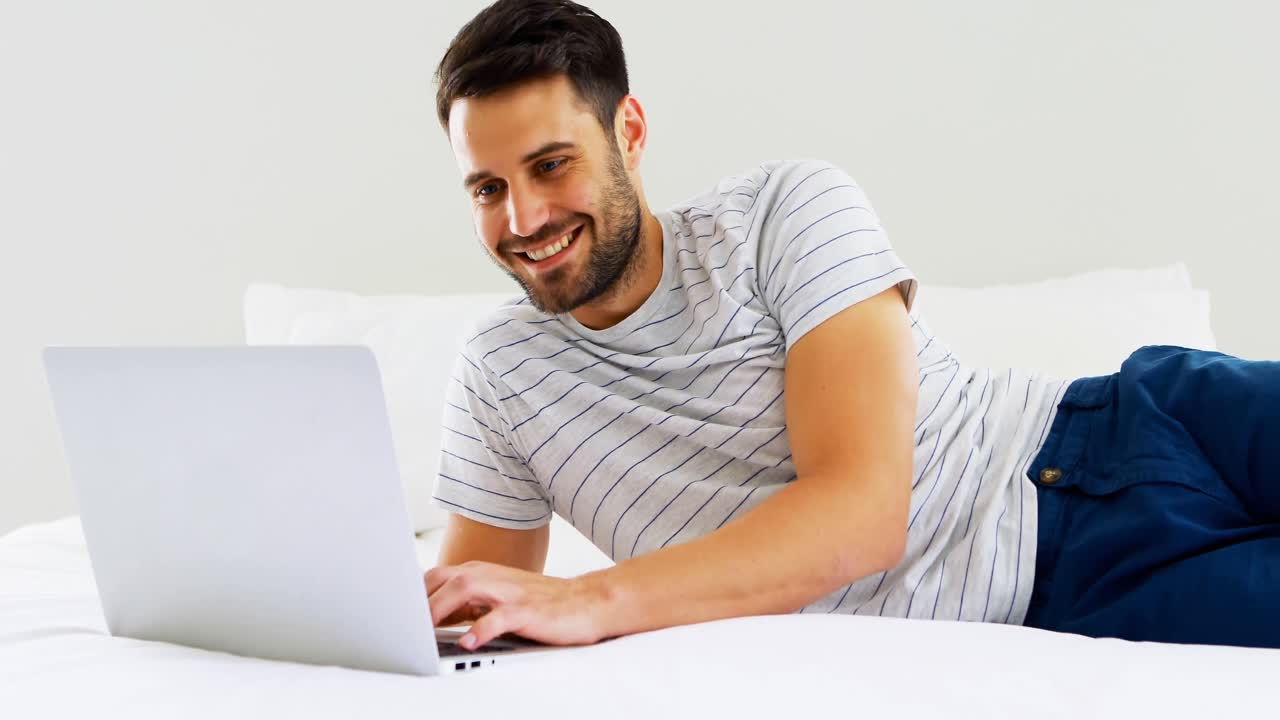 hombre usando computadora portátil en la cama en el dormitorio