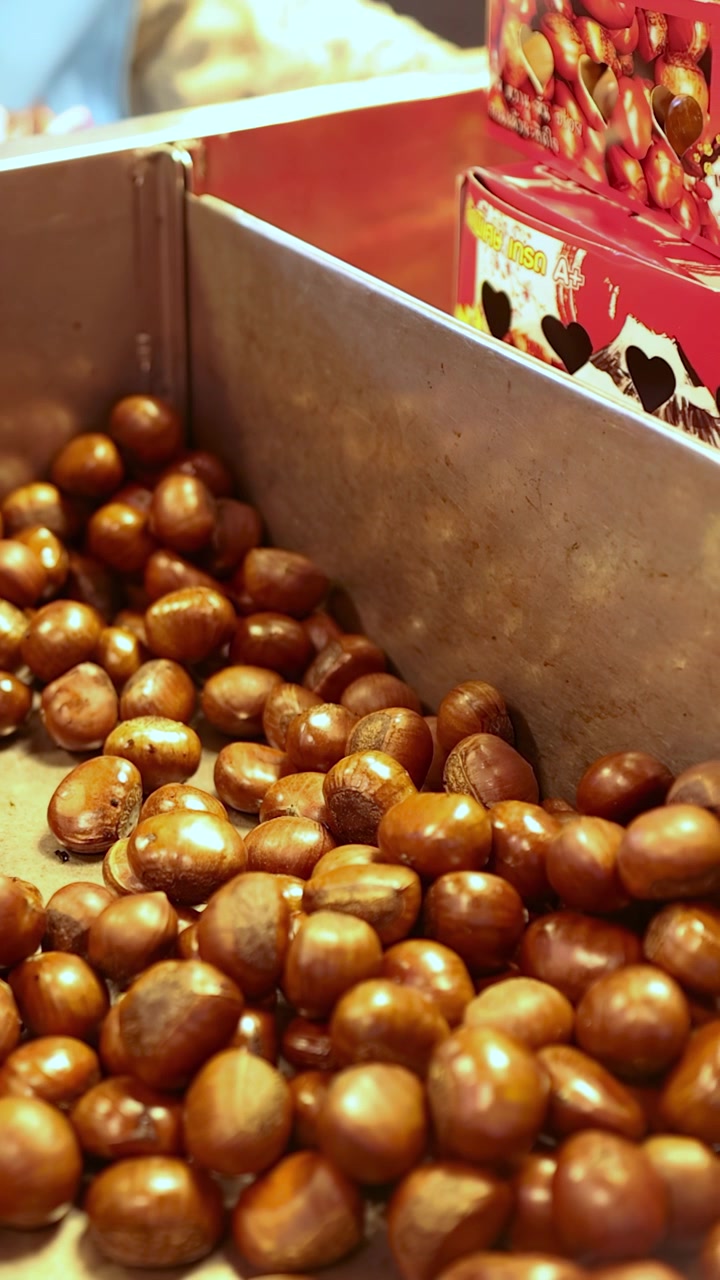 Castagne fresche mescolate in una padella di metallo, illuminazione calda, primo piano, mercato di strada.