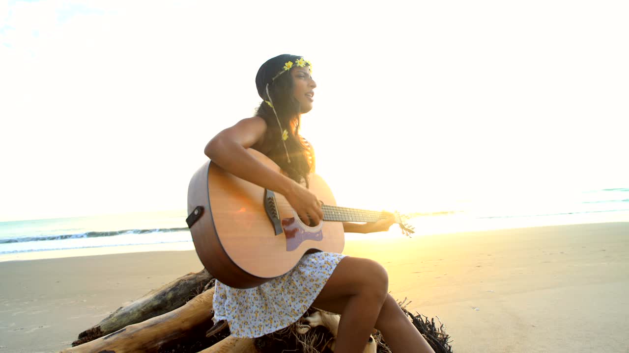 una mujer india asiática cantando tocando la guitarra en la playa.