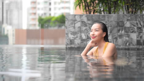 Una-Joven-Y-Atractiva-Mujer-Asiática-Relajándose-Dentro-De-Una-Piscina-En-La-Azotea-Al-Aire-Libre-En-Un-Balneario,-Pensando-En-La-Vista-Lateral-En-Cámara-Lenta