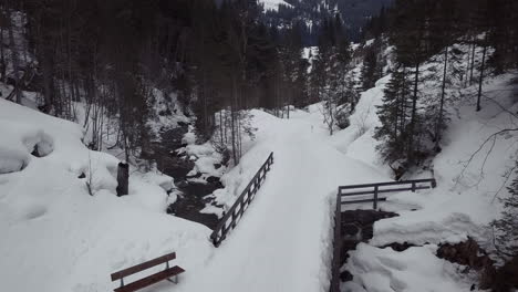 luftaufnahme einer kleinen brücke über einen bach in einem verschneiten tal in den alpen, kleinwalsertal, österreich