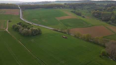 wide view drone footage of a tractor spraying large green pastures next to an asphalt road