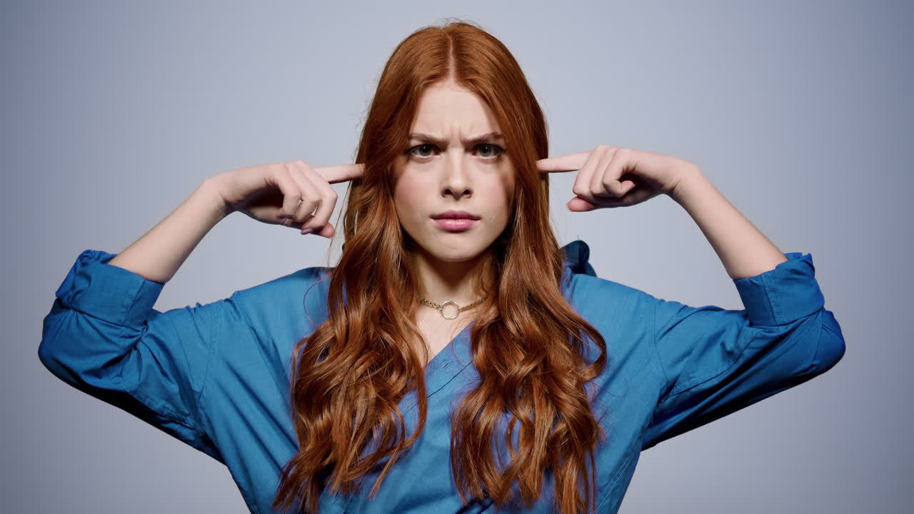 mujer preocupada poniendo los dedos en las orejas en el interior. chica mirando a la cámara en el estudio