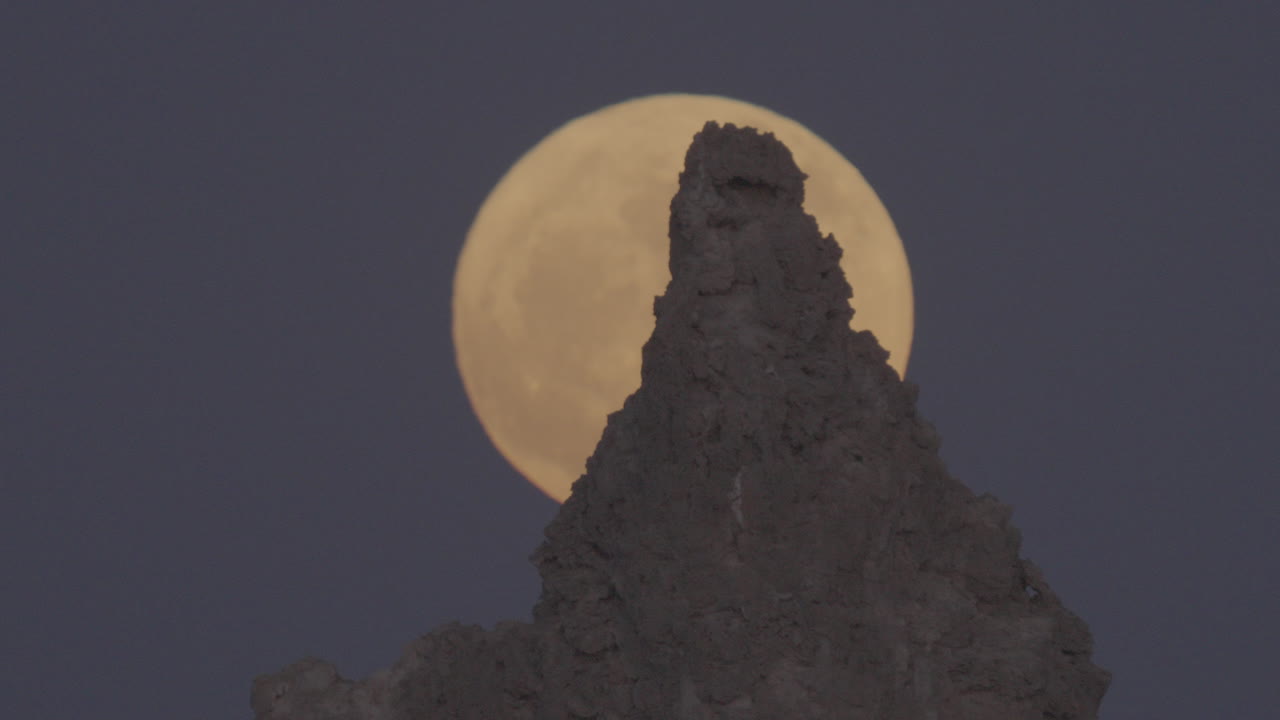 A de-focused full moon rises behind a rocky pinnacle outcrop in the desert night sky