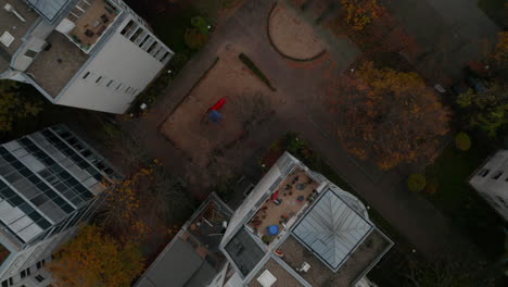 Vista-Escénica-Superior-De-Un-Patio-Trasero-Del-Barrio-Del-Gueto-Con-Tobogán-De-Juegos-Entre-Bloques-De-Apartamentos-Vista-Aérea-De-Pájaros-Arriba-Hacia-Abajo