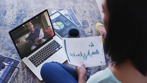 African-american-woman-holding-a-document-having-a-video-call-with-male-colleague-on-laptop