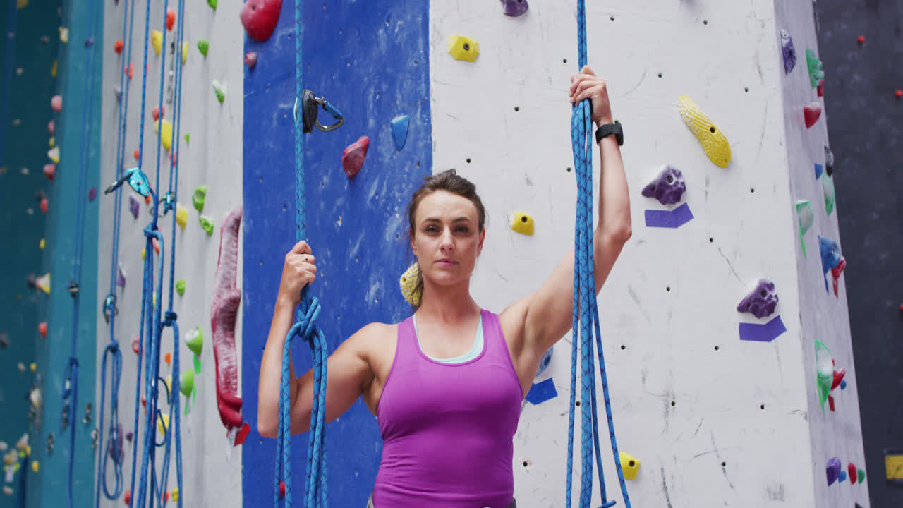 retrato de una mujer caucásica usando arnés y sosteniendo cuerdas en una pared de escalada interior