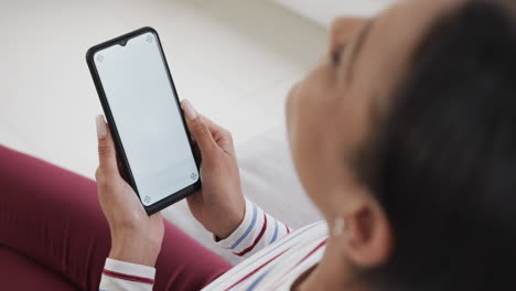 Mujer-Birracial-Sentada-En-Un-Sofá-Usando-Un-Teléfono-Inteligente-Con-Espacio-Para-Copiar-En-La-Pantalla,-Cámara-Lenta