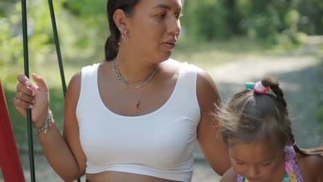 pregnant mother and daughter playing on swing outdoors