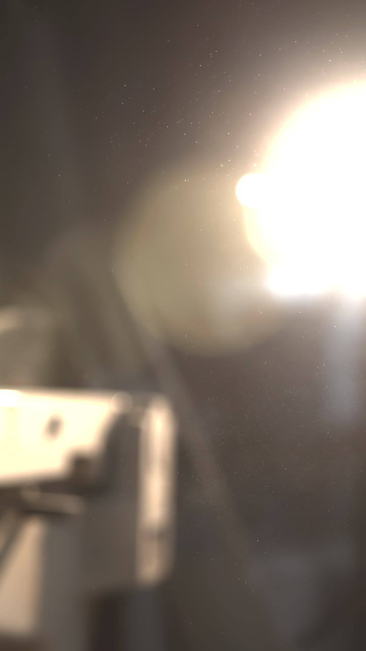 Lâmpada brilhante ilumina a borda da bancada, com reflexo quente da lente e partículas de poeira flutuantes, foco raso em uma prancha
