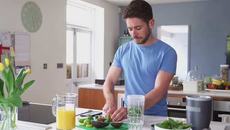 hombre haciendo una bebida de jugo saludable con ingredientes frescos en un exprimidor eléctrico después del ejercicio