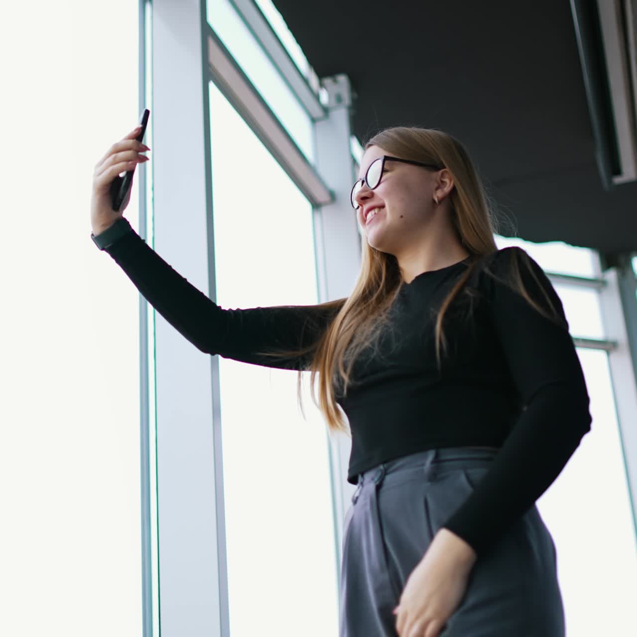 Happy female freelancer in formal wear with eyeglasses taking selfie on cellphone